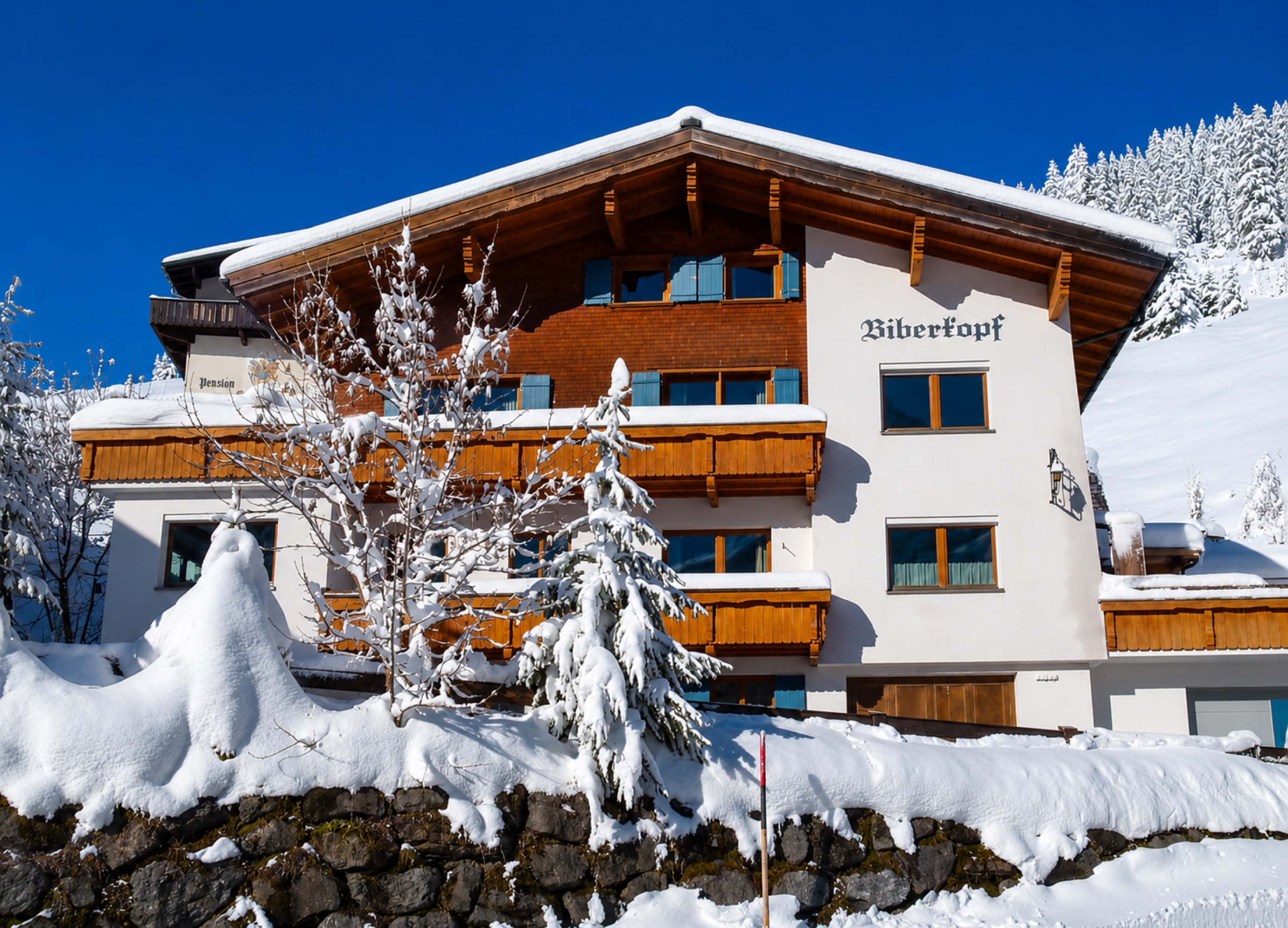 Haus Biberkopf in Lech am Arlberg – tief verschneit unter strahlend blauem Winterhimmel